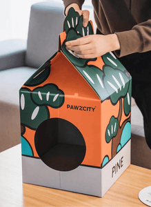 Hands assembling the Pine-themed Bonsai MilkBox Cat House, featuring Japanese bonsai tree illustrations.