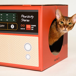 Cat looking out from red Pawzcity stereo cat house with circular side opening – retro-inspired cardboard furniture for cats.