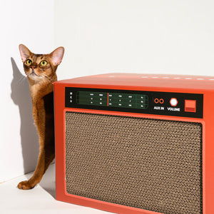 Brown cat standing beside red Pawzcity stereo scratcher – multi-functional design with durable corrugated cardboard.