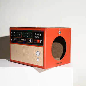 Side view of red Pawzcity stereo-style cat house – corrugated cardboard interior visible through circular entry hole.