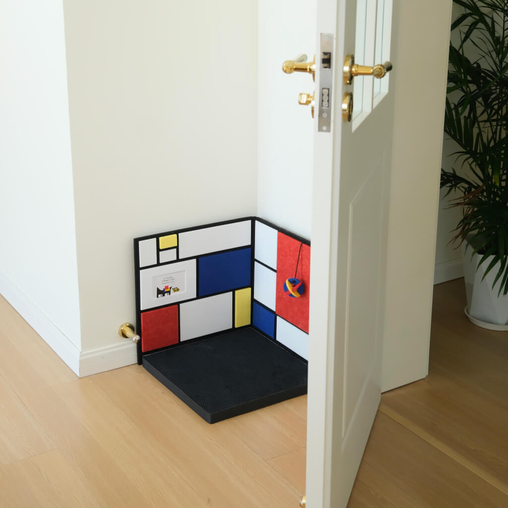 Corner cat scratcher placed behind open door — L-shaped wall protection with hanging toy and non-slip base.