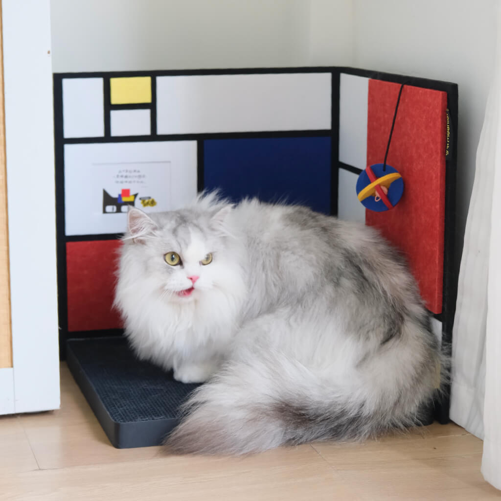 Cat using corner cat scratcher — Mondrian color-block panels, reversible walls, and floor mat base visible.