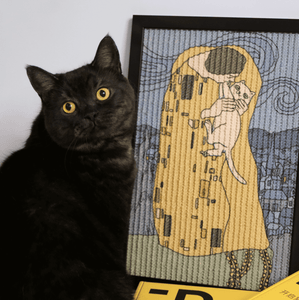 A close-up of a black cat next to a framed cat scratcher inspired by Klimt’s "The Kiss.