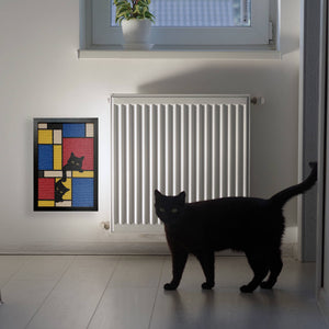 A framed Mondrian-style cat scratcher with geometric blocks and black cat illustrations mounted on the wall beside a radiator, with a black cat standing in the room.