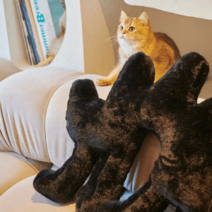 A cat sitting next to the Boom Boom Cat Cushion Black on a beige couch.