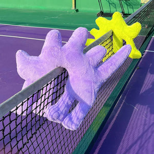 Gelato Purple and Fluo Green Boom Boom Cat Cushions perched on a tennis net.