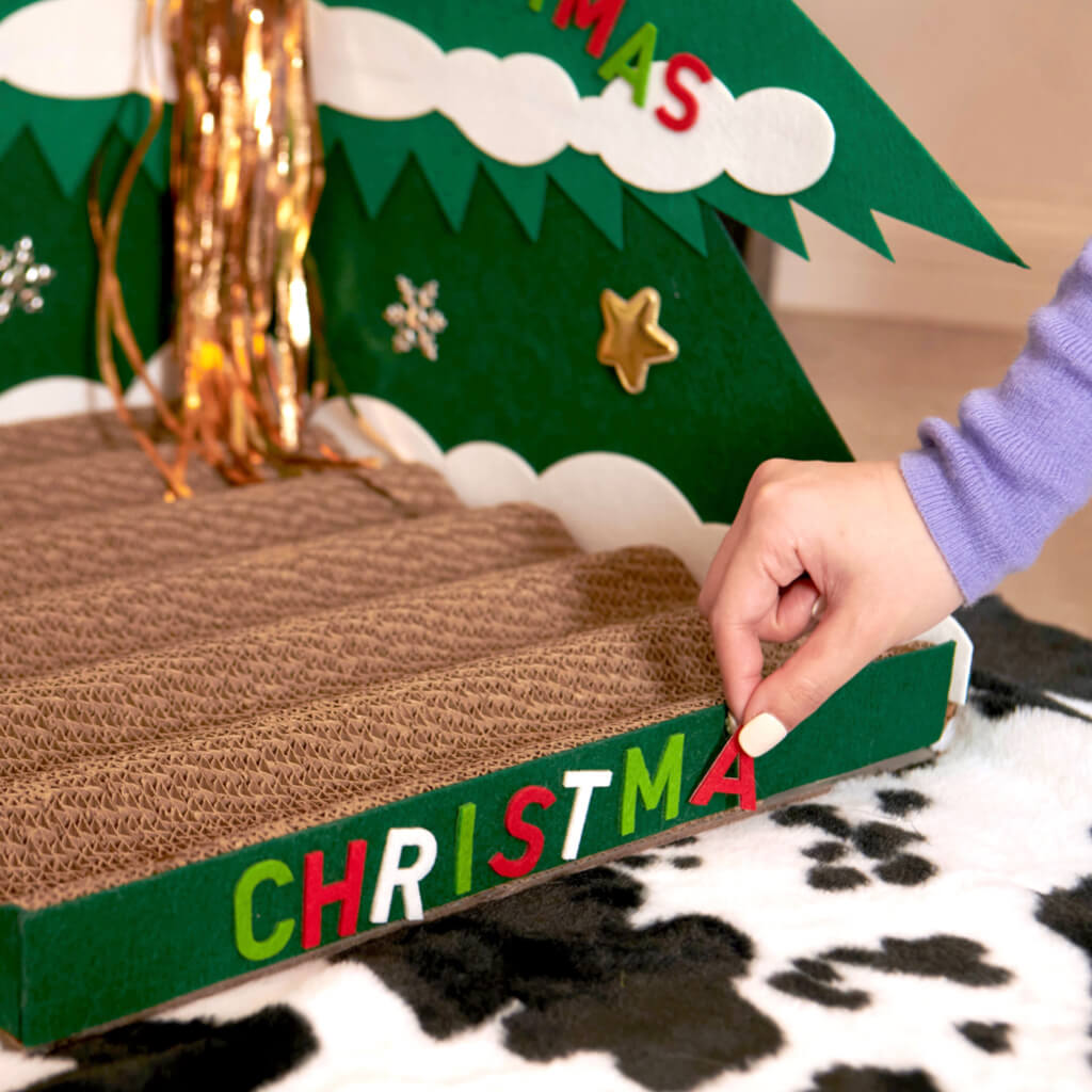 Close-up of a person adding Christmas letters to the Cat Scratcher base.