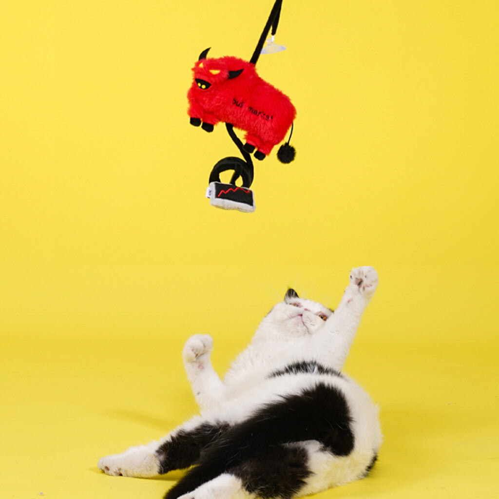 Red plush bull market cat toy hanging with suction cup as cat reaches up to play.