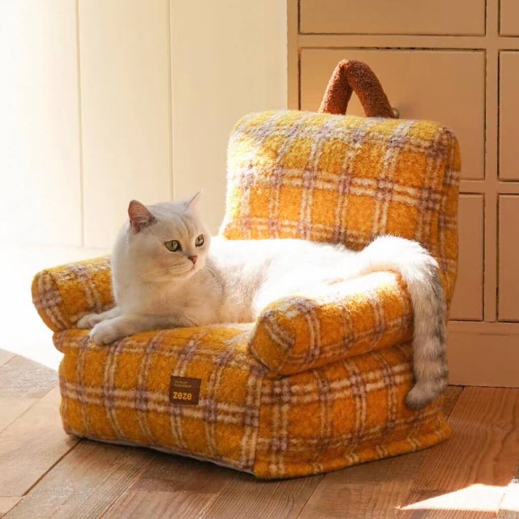 White cat relaxing on a yellow plaid armchair-style pet sofa with carry handle.