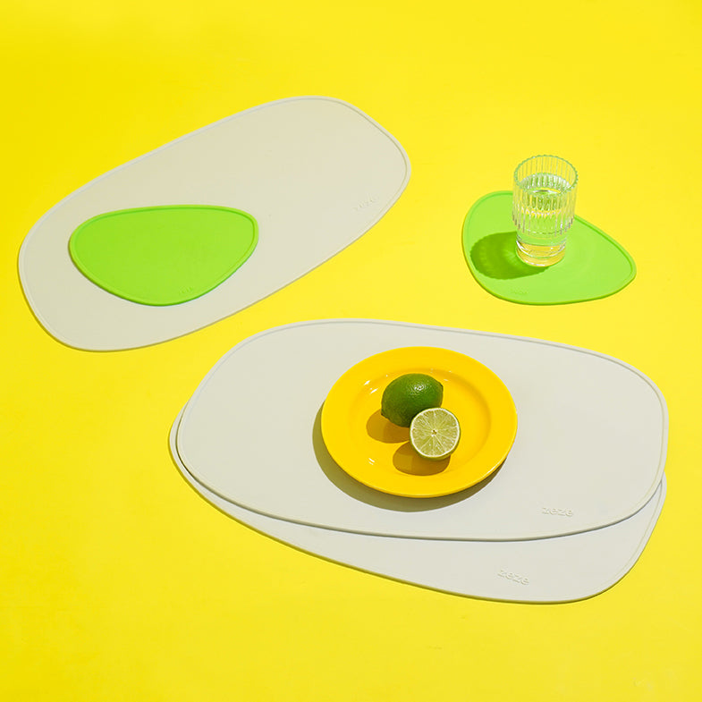 Green and white abstract silicone placemat set with a glass of water on a bright yellow surface.