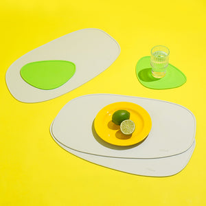 Green and white abstract silicone placemat set with a glass of water on a bright yellow surface.