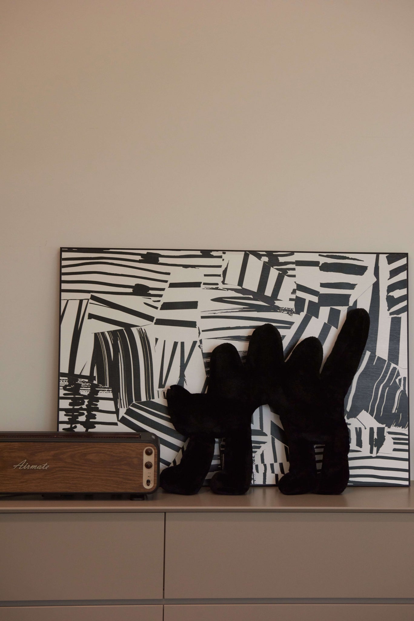 The black Boom Boom Cat Cushion placed on a white cabinet against a black-and-white abstract art backdrop.