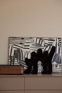 The black Boom Boom Cat Cushion placed on a white cabinet against a black-and-white abstract art backdrop.