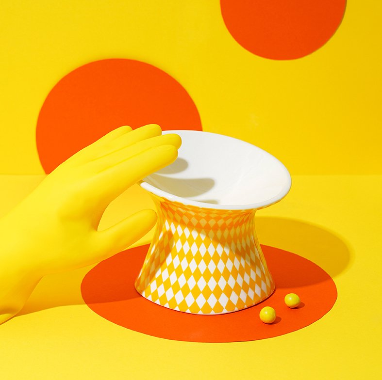 Yellow-gloved hand cleaning the ZEZE Elevated Ceramic Bowl - Yellow Rhombus under water, highlighting the easy-to-clean surface.